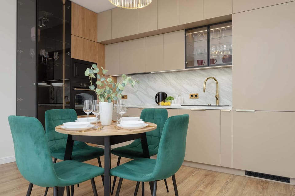 A round glass dining table surrounded by stylish green chairs. Bright accents, including lemons and plants, make the space inviting.