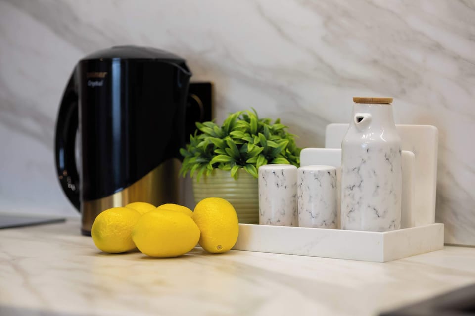 A close-up of a black electric kettle placed beside lemons and herbs on a marble counter. Functional items double as décor.