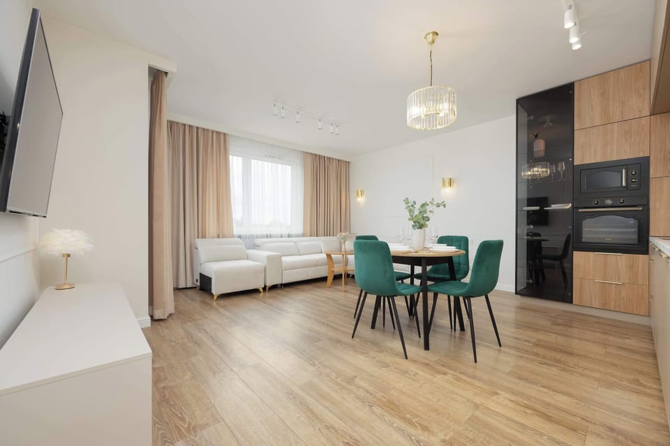 Another angle of the living and dining space with a sofa, chairs, and large windows. The open-plan layout enhances the sense of space.