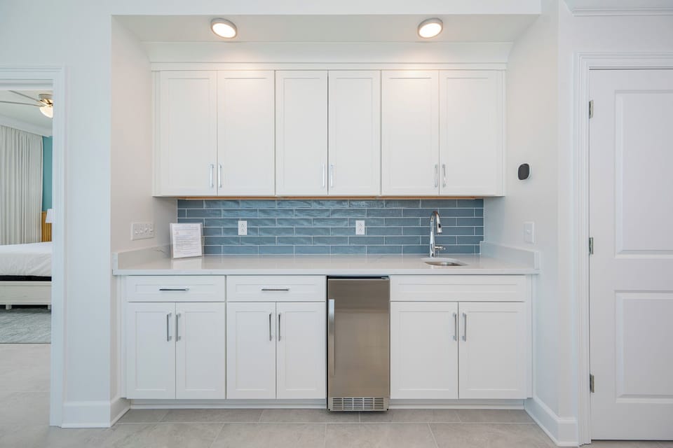 Prepare snacks and drinks at thw wet bar, featuring a stainless mini-fridge and a stylish backsplash