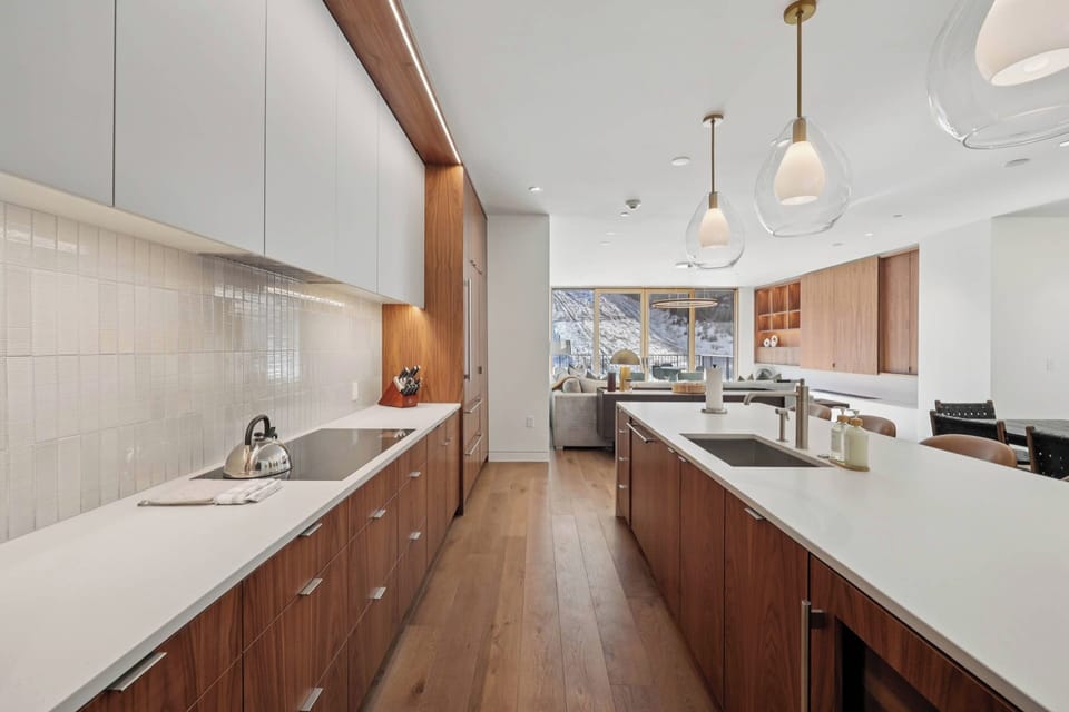 Your modern kitchen features warm wood cabinetry, sleek white countertops, and pendant lighting perfect for preparing mountain getaway meals.