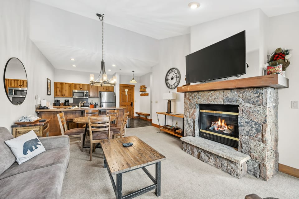 Living with bear pillow, oversize clock, and open kitchen.
