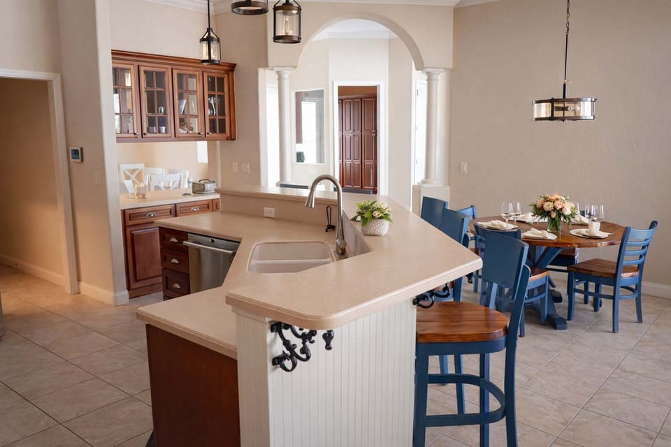 Open kitchen with a breakfast bar and adjacent dining area featuring blue chairs and a round wooden table.