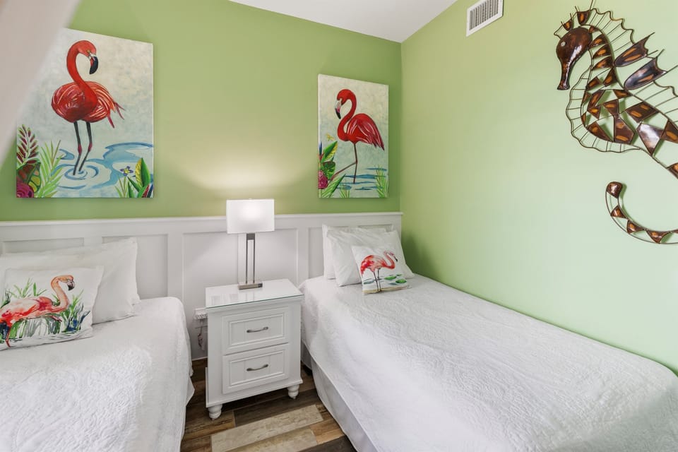 Wake up refreshed in your tropical twin bedroom, where playful flamingo art and soothing green walls create a cheerful seaside escape.