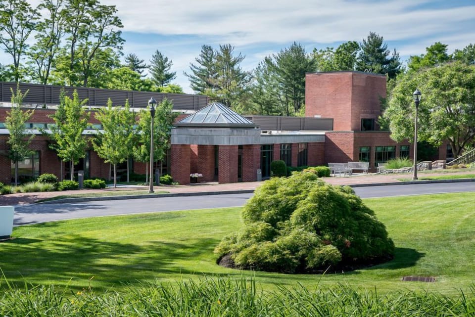 A serene view of Windrose’s landscaped grounds highlights orderly trees and a well-maintained facade, creating a peaceful environment perfect for relaxation.