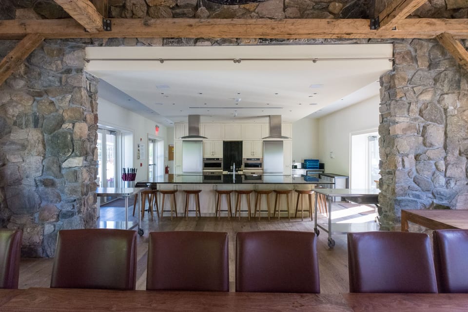 The modern meeting space at Windrose boasts an inviting atmosphere, highlighted by natural light and rustic stone accents, perfect for gatherings or culinary classes.