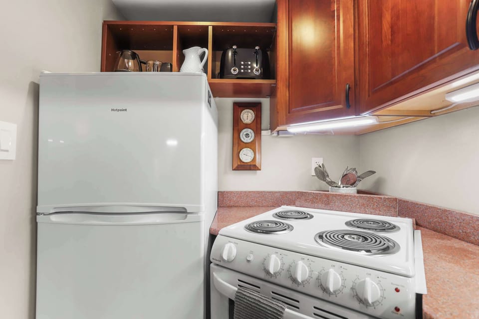 View of kitchen appliances like fridge gas range oven, toaster, coffee maker and overhead wooden cabinets,