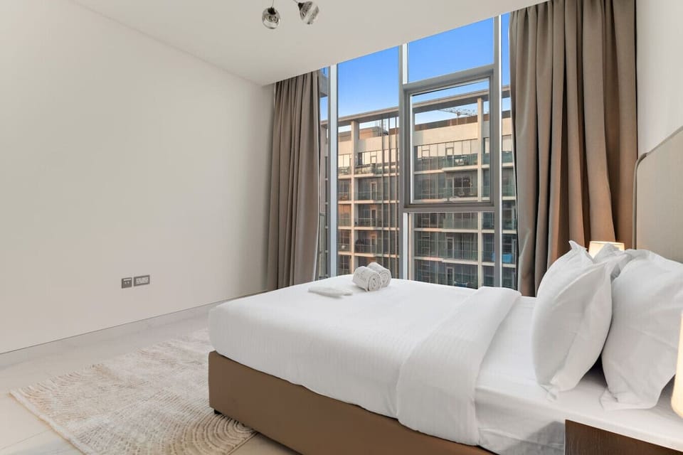 Bright bedroom with floor-to-ceiling windows and neutral-toned curtains.