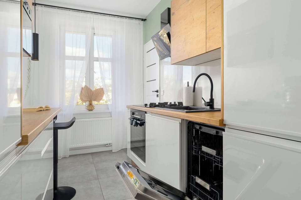 A compact kitchen featuring modern appliances, white cabinets, and a wooden countertop.