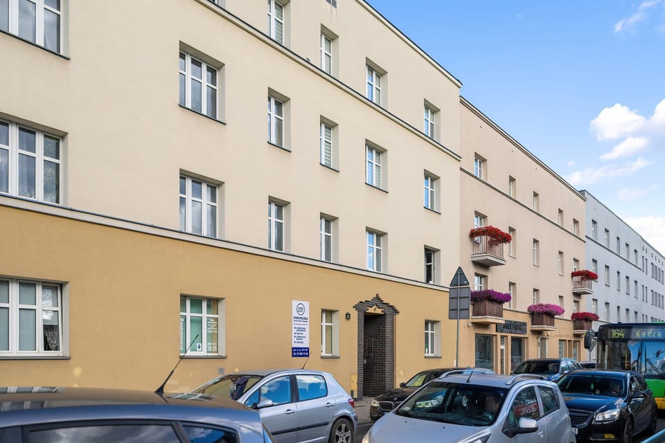 A street view of the building exterior with pastel-colored facades and parked cars.