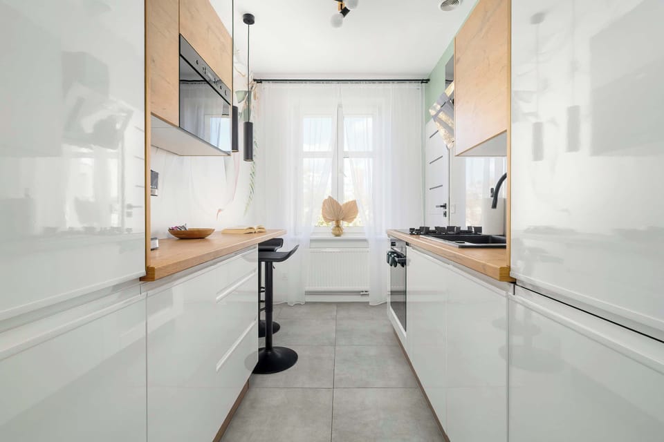 A full kitchen shot with white and wooden cabinets, window light, and modern appliances.
