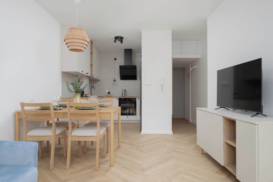 A dining area with a table set for four and the living room visible in the background. The space is bright, cheerful, and ready for meals.