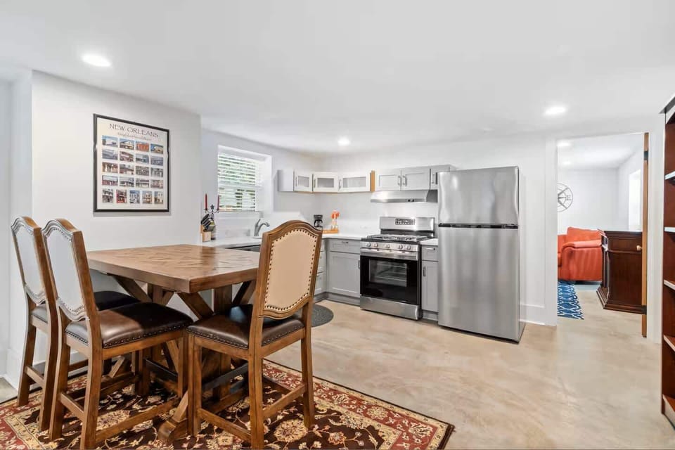A warm wooden dining table with seating for four sits beneath bright windows, just steps from the cooking space.