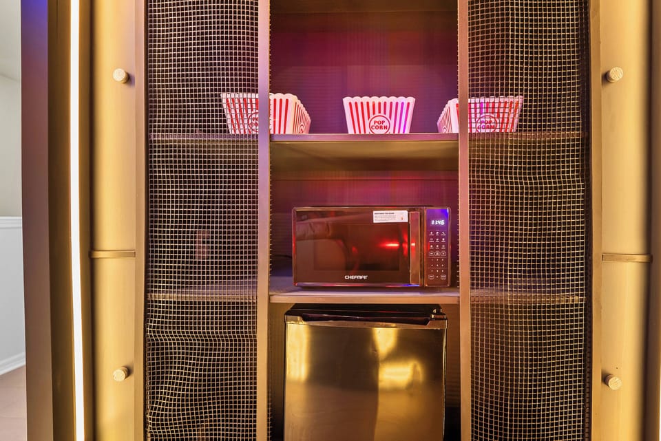 This stylish kitchenette boasts a sleek microwave and stainless steel refrigerator in a chic cabinet, complemented by thoughtfully arranged popcorn bowls—perfect for your cozy movie nights. Enjoy your stay!