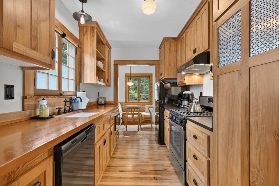 Glowing galley kitchen with wood countertops, floors, modern appliances, and a sunny dining nook by the window.