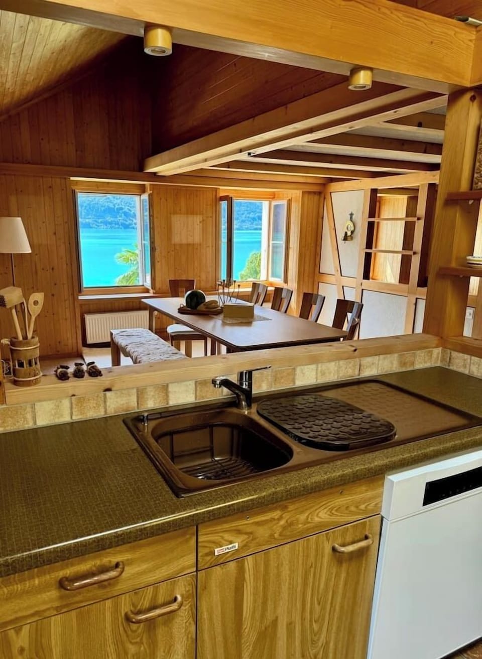 Fully equipped alpine kitchen with sink, dishwasher, and direct view into the dining area and Lake Brienz