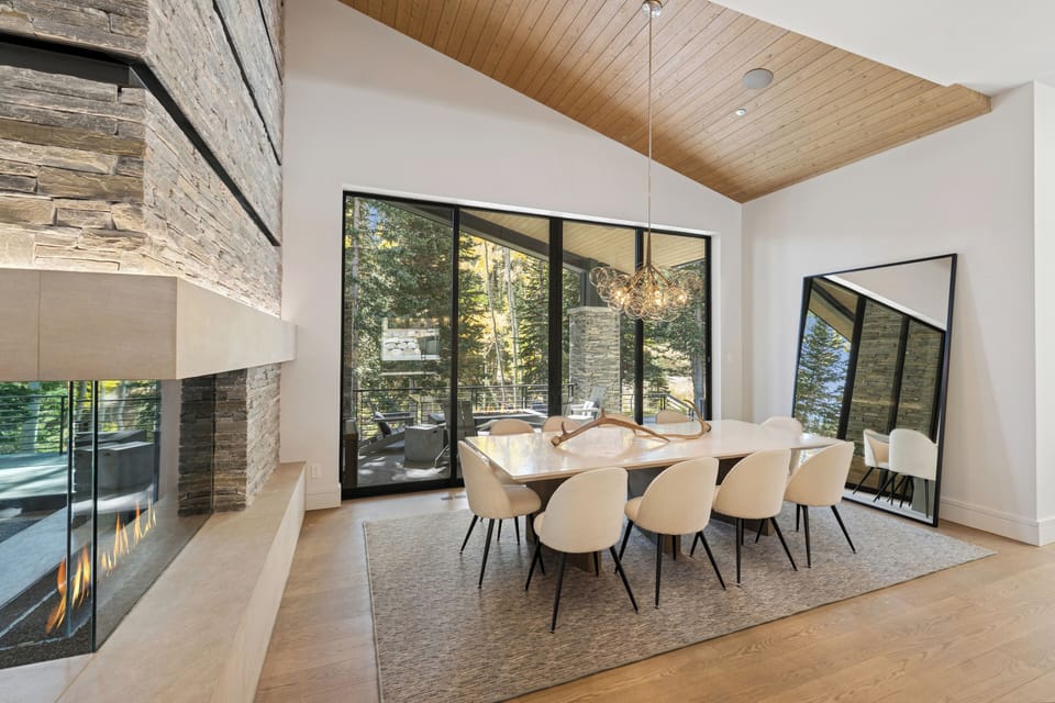 Elegant dining room with modern lighting, high ceilings, and forest views