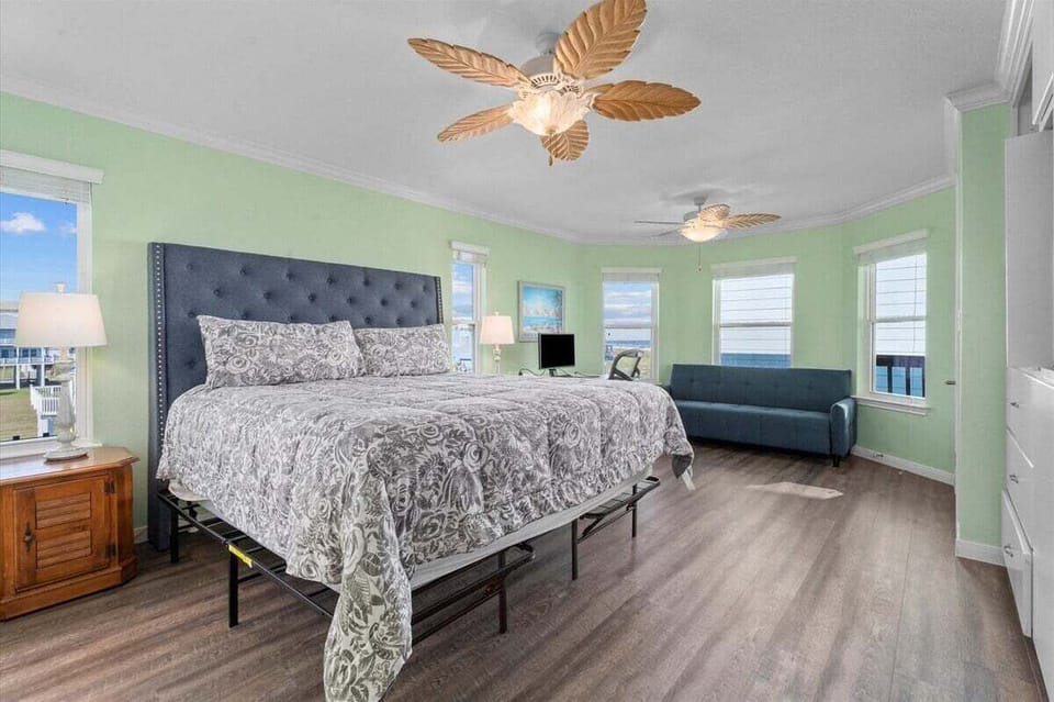 Spacious bedroom with large bed, ceiling fan, TV, windows, and sitting area for relaxing after beach days.