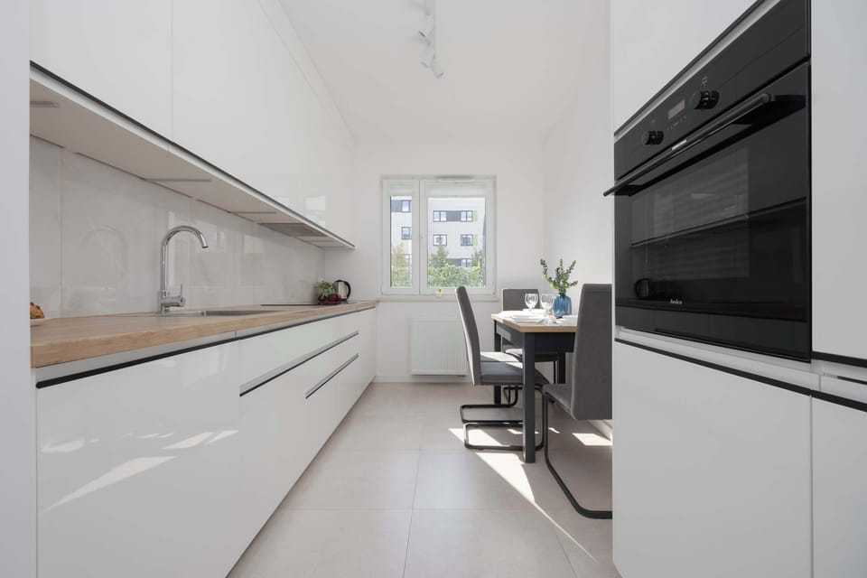A modern kitchen in white with wooden accents and a wide countertop. The long layout offers plenty of cooking space.
