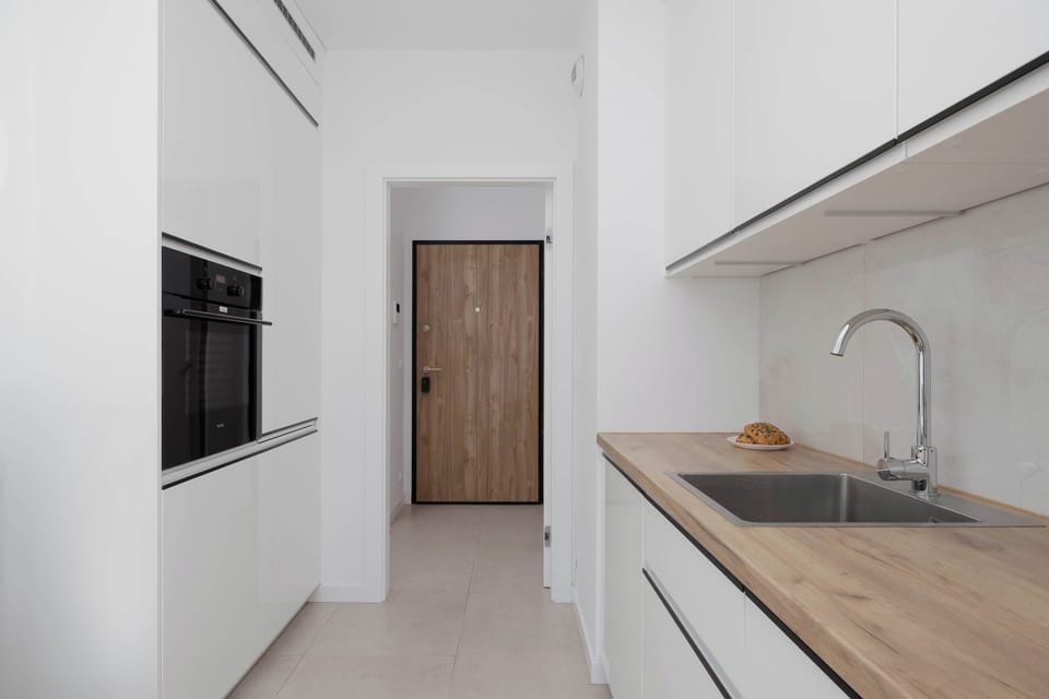 A narrow white kitchen with wooden accents and modern appliances. The layout makes it both practical and visually appealing.