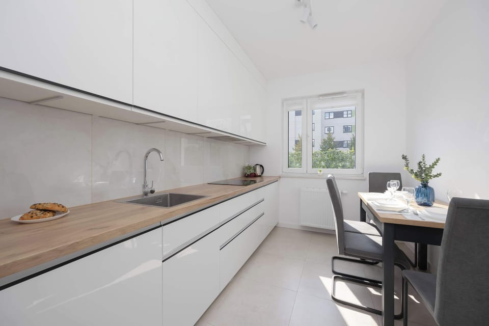 A sleek white kitchen with wood countertops and a window for natural light. Minimalist cabinets provide a clean, uncluttered look.
