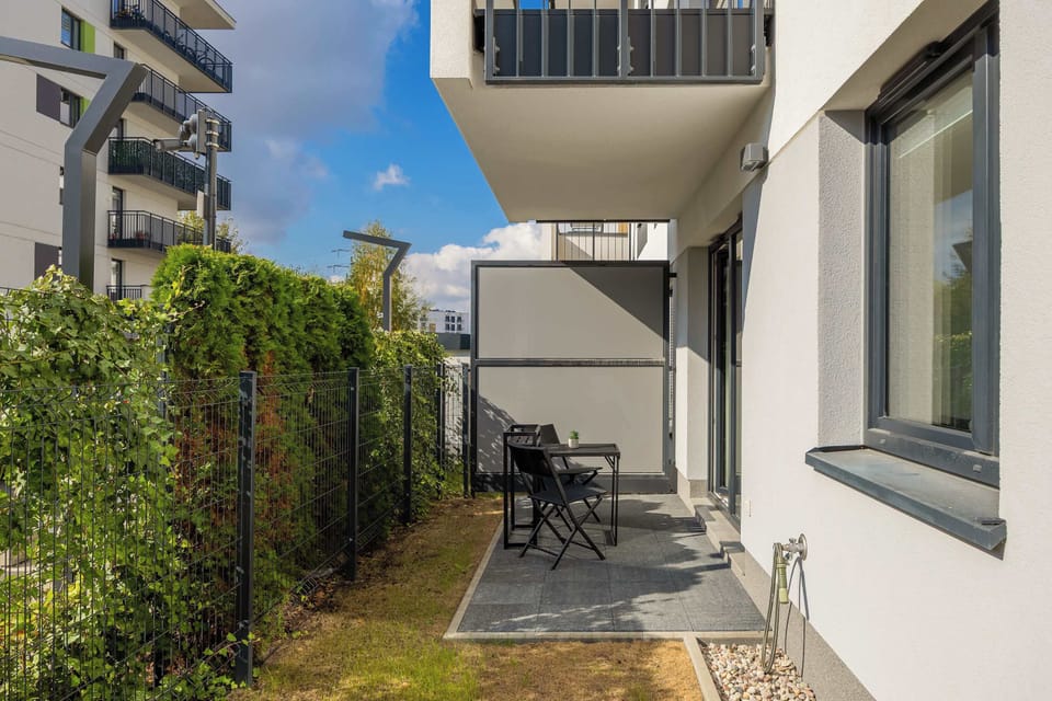 A small garden with outdoor furniture and a green hedge. The space feels private yet open to the outdoors.
