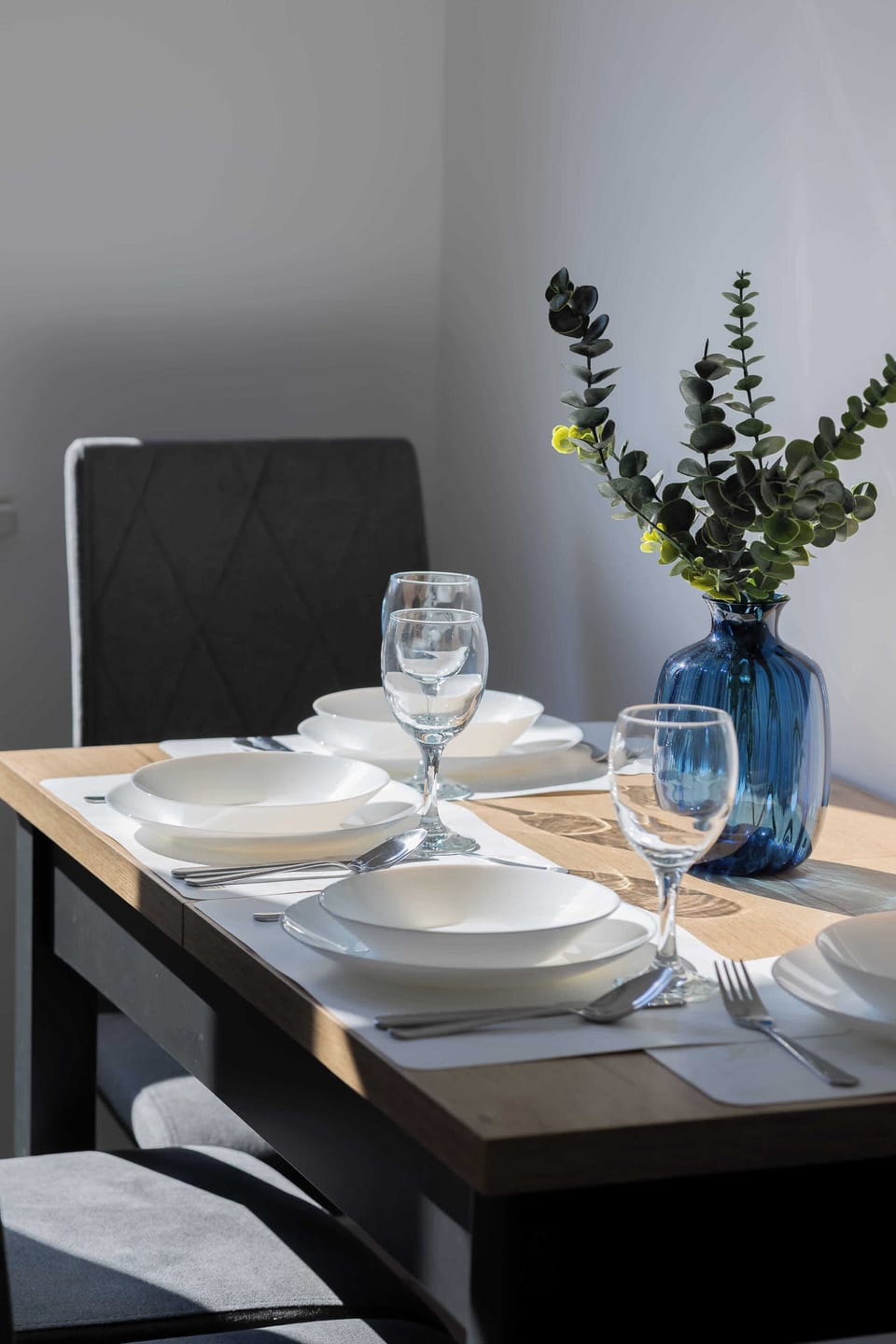 A dining table with two plates, cups, and a vase with flowers. The setup is intimate, perfect for a small meal.