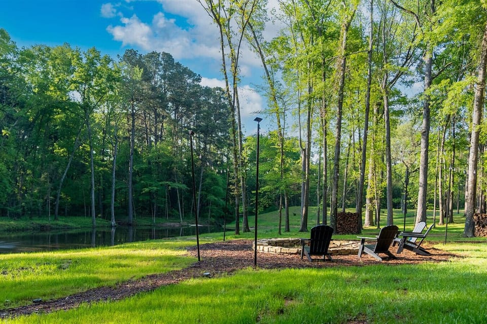 Outdoor fire pit with Adirondack chairs set beside the pond in a quiet, wooded setting.