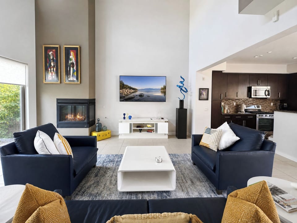 Sink into plush navy sofas beside a cozy fireplace, with modern art and lake views inviting relaxation. Your open kitchen awaits nearby for effortless entertaining.