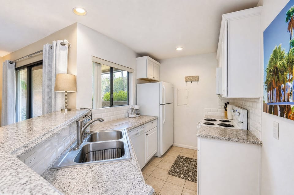 A bright, fully-equipped galley kitchen features granite countertops, white cabinetry, and modern appliances, ready for your home-cooked vacation meals.