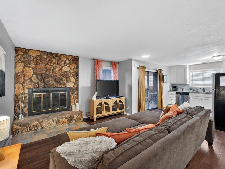 Cozy lounge with stone fireplace, big sectional, and open kitchen.
