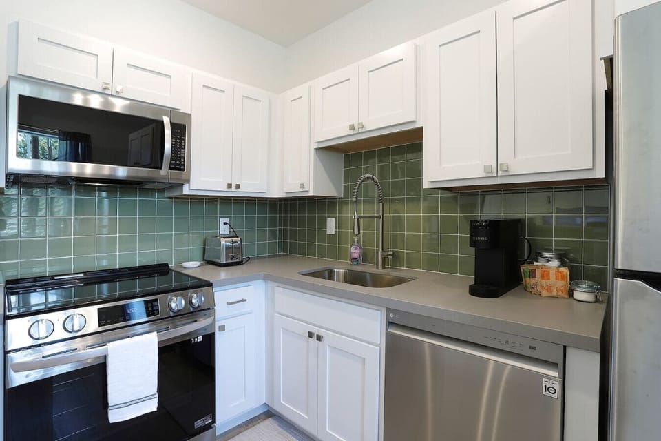 Fully equipped kitchen featuring stainless steel appliances - microwave, full-size refrigerator, dishwasher, modern stove with oven, and a high-arc pull-down faucet. Perfect for cooking meals or enjoying morning coffee together.