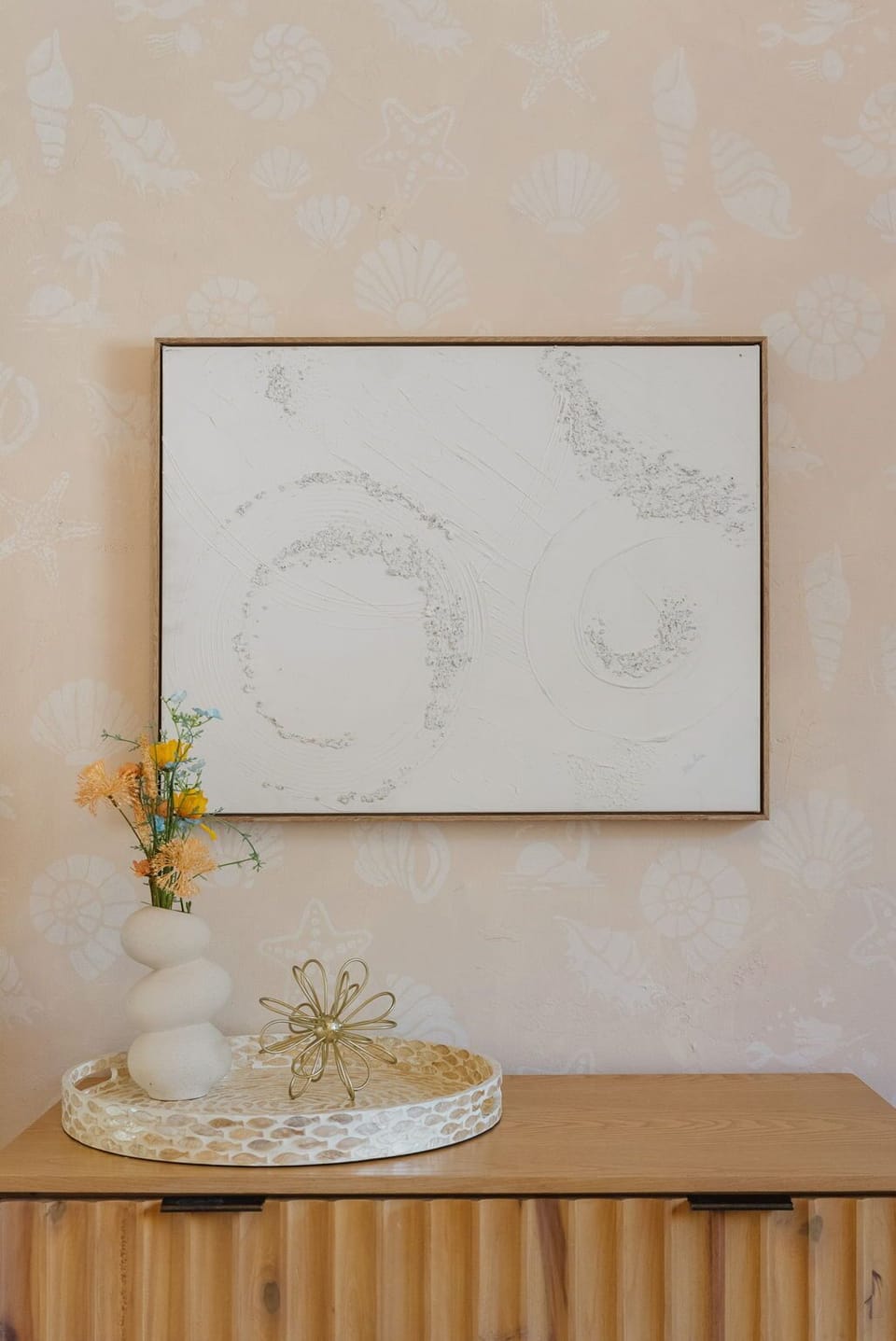 Minimal dresser setup with soft decor and textured wall art above.