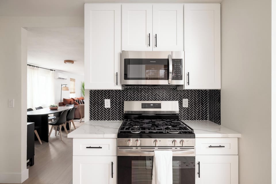 Modern kitchen with stainless steel stove and microwave, sleek backsplash. 