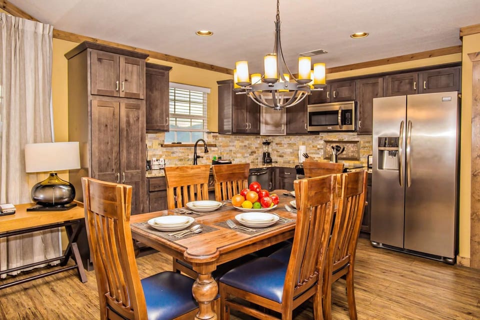 Dining area with wooden table, chandelier, and adjacent full kitchen.