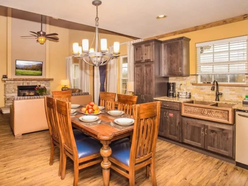 Dining area with wooden table and chandelier adjacent to kitchen.