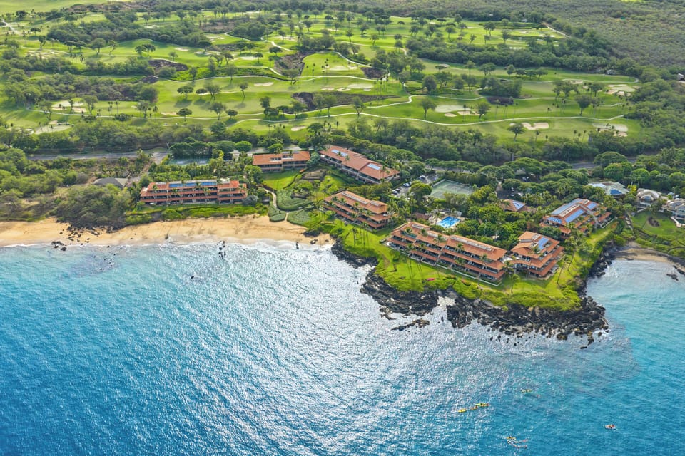 Stunning aerial view of a coastal resort nestled between pristine beaches and a championship golf course, offering an idyllic Hawaiian setting surrounded by tropical landscapes and azure waters.