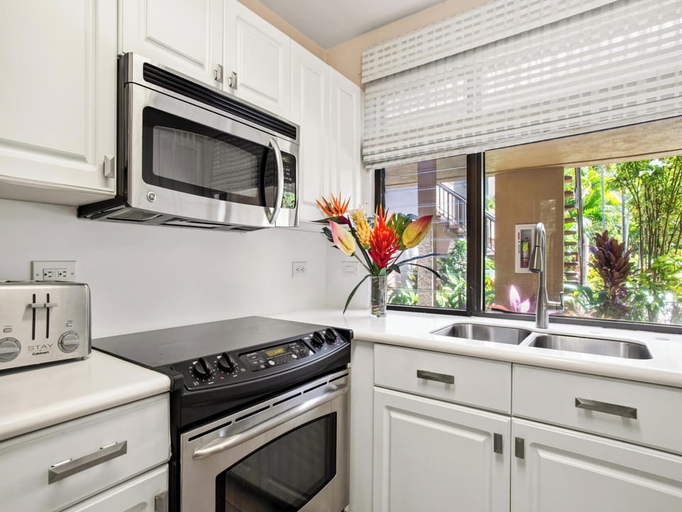 Your bright, well-equipped kitchen features stainless steel appliances and tropical garden views through the window, creating a fresh and inviting space for preparing meals.