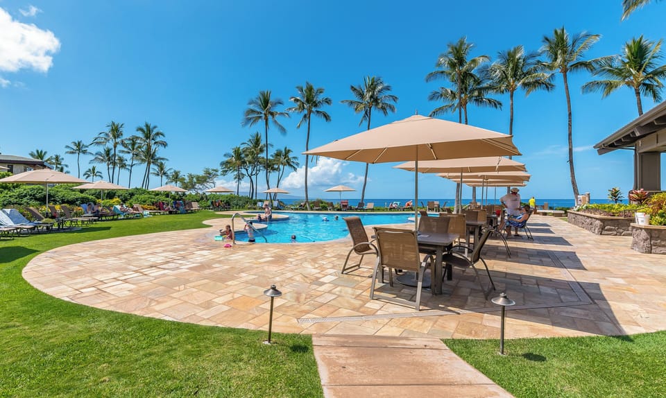 The property features an oceanfront pool surrounded by palm trees, with panoramic views of the Pacific. Expansive patio areas and manicured lawns provide ample space for relaxation and outdoor entertainment.