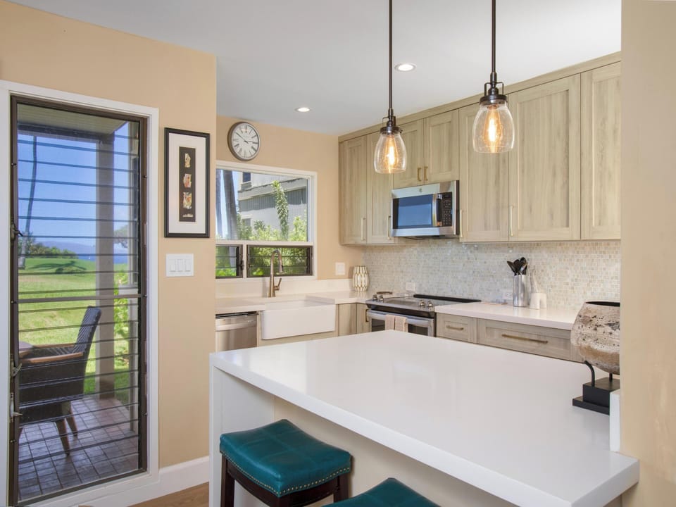 Gather around the bright island with stylish pendant lighting and farmhouse charm. Sleek countertops and natural light make meal prep a breeze, while the door opens to peaceful outdoor views.
