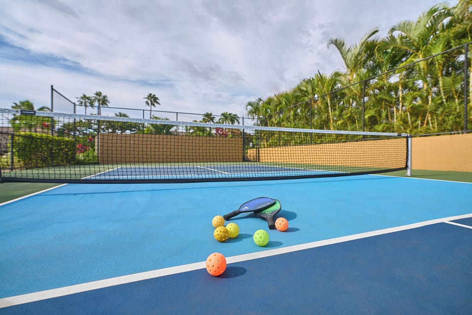 A pristine pickleball court awaits your friendly matches, complete with paddles and balls ready for play. Palm trees sway overhead as you enjoy sunny days perfecting your game.