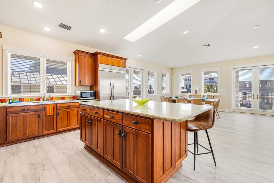 Spacious kitchen featuring wood cabinetry, large center island, stainless appliances, and high ceilings with natural light