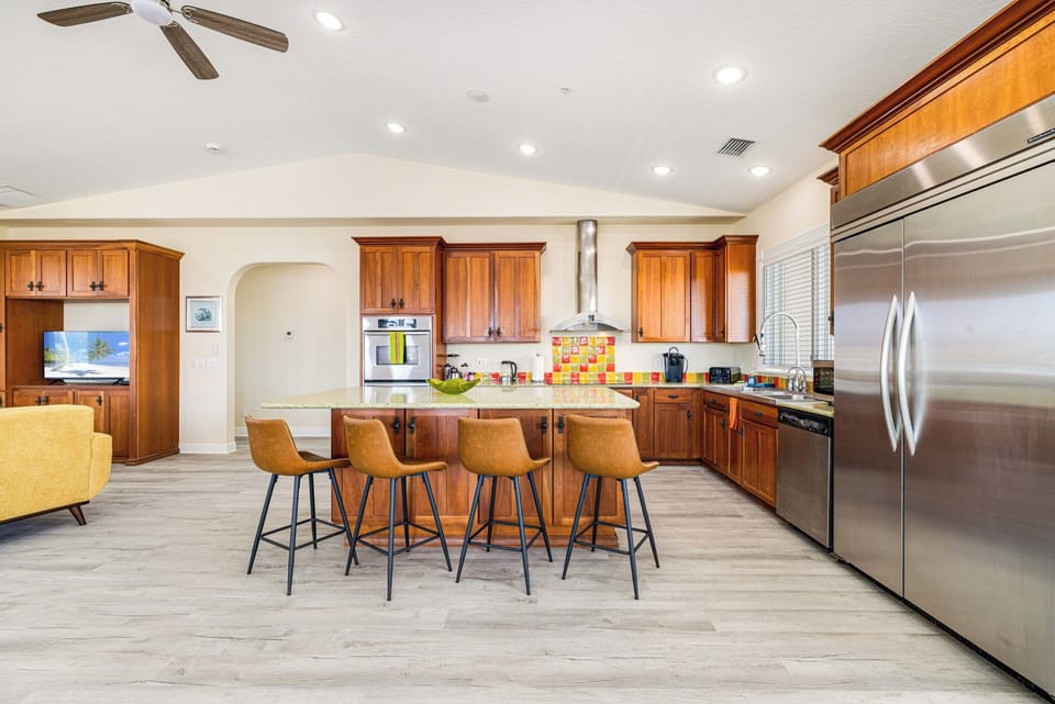 Kitchen featuring wood cabinetry, large granite island with bar stools, and stainless steel refrigerator