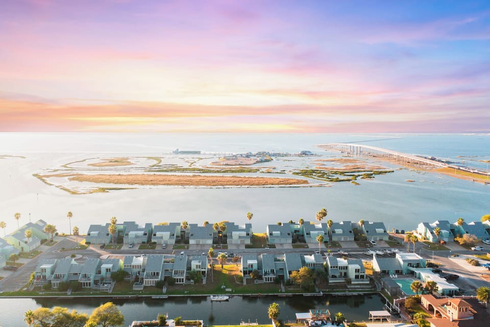 Stunning aerial view showcases the waterfront community and scenic bridge spanning across tranquil waters under a breathtaking sunset sky.