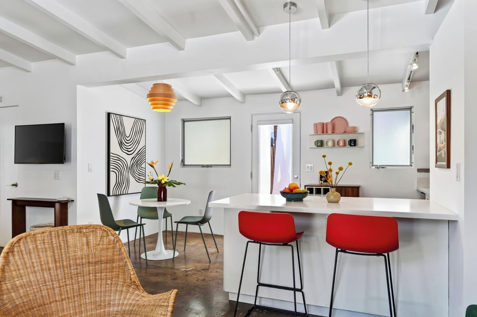 A bright open layout connects the kitchen and dining area, with bold red barstools and playful mid-century style throughout.