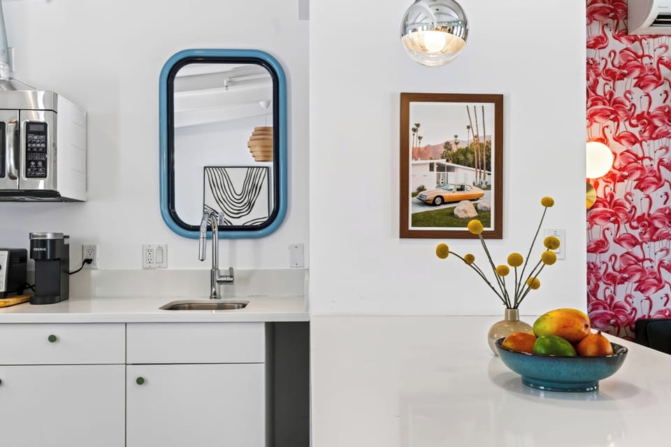 A sleek kitchenette gets a retro touch from the blue-framed mirror and vintage-inspired accents, keeping the studio both stylish and functional.