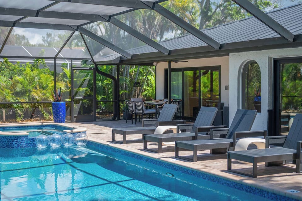 Enjoy the sparkling pool and hot tub on the screened lanai, surrounded by lush tropical greenery and comfortable seating.