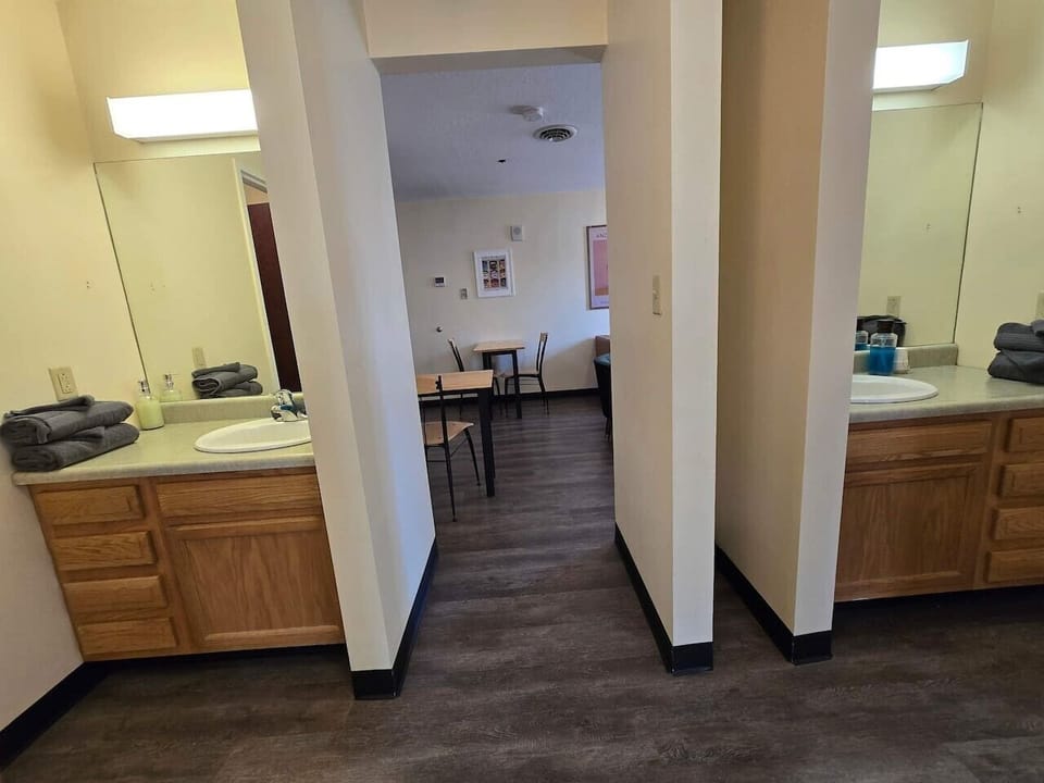 Two separate vanity areas w/ wood cabinetry, sink & fresh towels, framing a view straight into the dining space.