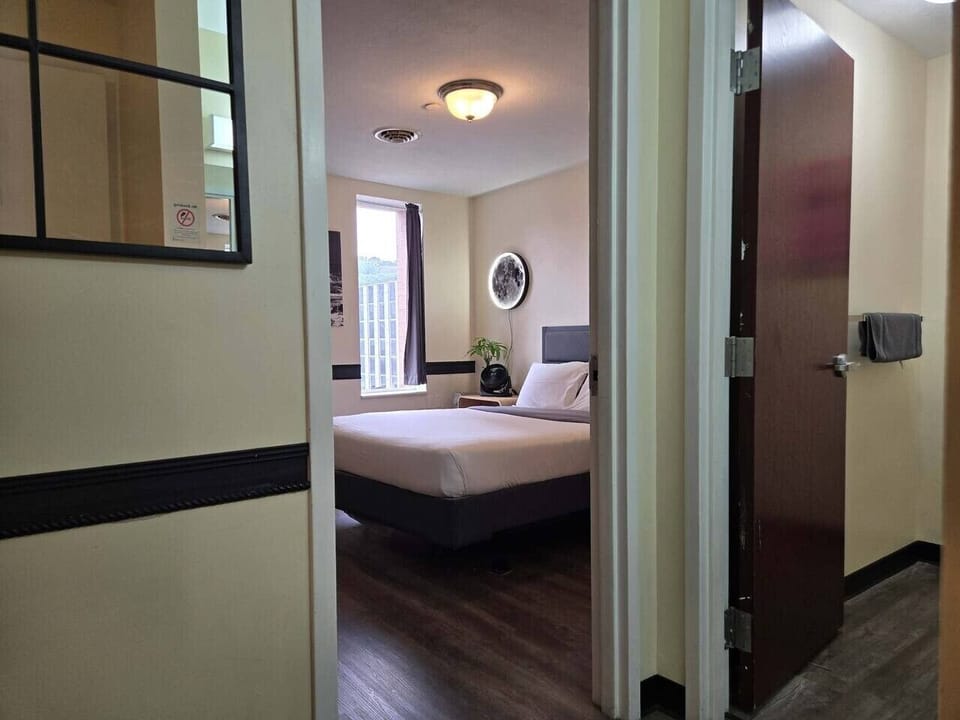 Bedroom w/ bed, mirror & wall art, bright & window-lit.