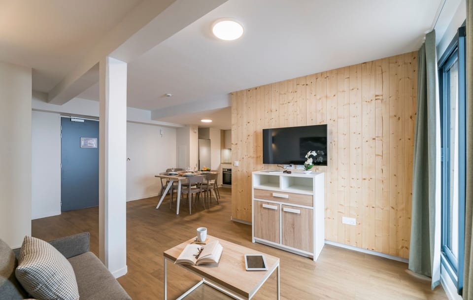 Experience the charm of this open living space, complete with wooden accents, a large TV, and a sunlit ambiance that invites relaxation and comfort.